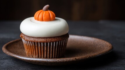 Delicious pumpkin cupcake with creamy frosting and decorative fondant icing on a rustic plate against a dark background