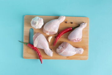 Pieces of fresh chicken drumstick, garnished with red pepper and garlic, on a wooden stand close-up view from above
