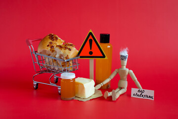 The concept of the great danger of products containing trans fats. A doll, warning signs and the inscription "trans fats on a dark red background