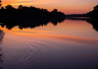 Serene sunset over calm river reflecting fiery orange and purple sky and silhouetted trees