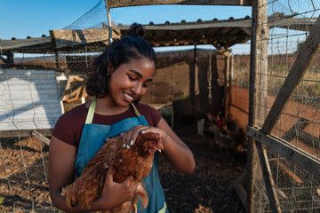 Young farmer woman holding a hen in a chicken coop