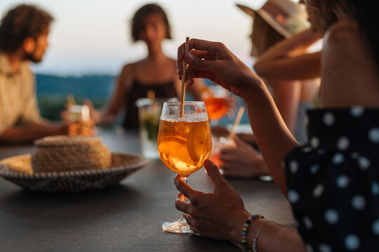 Woman holding aperitif cocktail at sunset party with friends