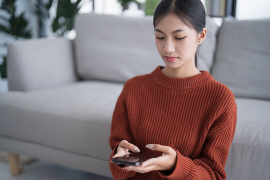 Asian Woman controlling smart home. mobile phone with smart home app in living room. touch screen ai technology. Remote home control system