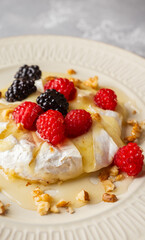 Melted camembert cheese topped with raspberries, blackberries, walnuts and honey. Healthy dessert. Shallow depth of field.