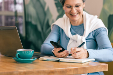 Middle-aged woman working online with laptop and coffee cup