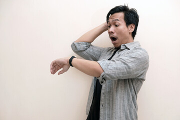 Southeast Asian man wearing flannel shirt holding a watch and shocked expression, on white isolated...