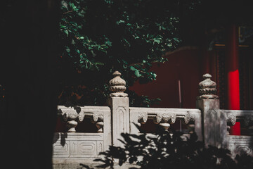 A serene view from The Palace Museum in Beijing. Stone fence foliage frame a red wall, bathed in...