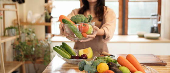 A woman is holding a bowl of vegetables in a kitchen. Concept of health and wellness, as the woman is surrounded by fresh produce