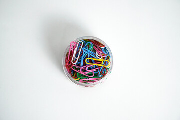 A clear plastic jar filled with a mix of colorful paper clips, isolated against a white background. This image is perfect for concepts of office supplies, organization, creativity, and business tools.