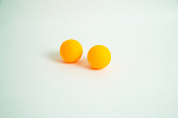 Two bright orange table tennis balls sit side-by-side on a white surface. The simple and clean composition is perfect for concepts of sports, recreation, games, or equipment.

