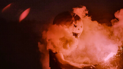 Halloween human pumpkin or Jack o lantern costume on a dark night with lots of smoke, a chainsaw,...