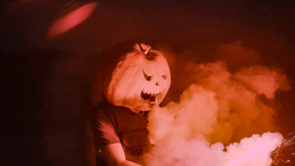 Halloween human pumpkin or Jack o lantern costume on a dark night with lots of smoke, a chainsaw,...