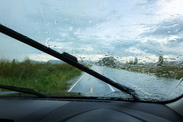 View from inside a car during a rainy drive on a rural road, with wiper clearing water to reveal a clearer path ahead © patpitchaya