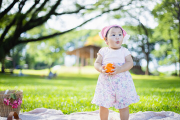 Family enjoys leisure picnic in green park where little child holds orange fruit while people relax nearby creating warm and joyful concept of outdoor fun and togetherness