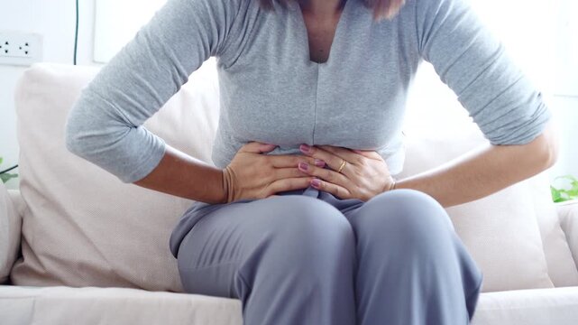 Asian woman suffering from stomachache and abdominal pain during menstruation, also relatable to diarrhea or food poisoning
