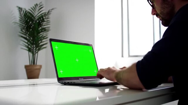 Man Working on Laptop with Green Screen in Office.
