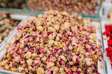 A close-up view of a market display filled with dried rosebuds in pink and cream tones, often used for tea, potpourri, or natural remedies.
