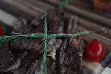 Pieces of dried smoked fish with rosemary and cherry tomatoes on a wooden board.