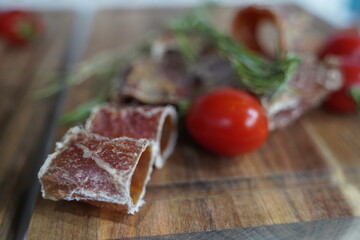 Pieces of dried smoked fish with rosemary and cherry tomatoes on a wooden board.