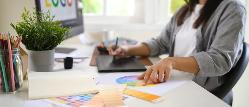Female designer choosing colors from chart while using graphic tablet, creative process in home office
