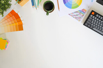 Top view of creative designer workspace with color palette, and coffee cup on white desk
