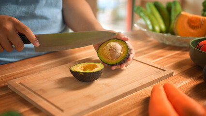 Close up of person slicing avocado in half on cutting board, preparing fresh ingredients for healthy meal