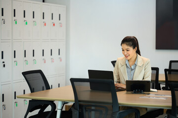 Asian woman in beige suit using laptop and digital tablet in coworking space
