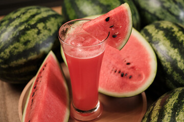 Close-up shot of half pieces of fresh red watermelons and glass of smoothie on wooden dish, natural...