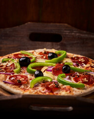 Pizza with chorizo ​​sausage, mozzarella cheese, green pepper and black olives. Rustic wooden background. Soft focus.	