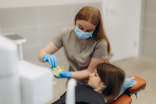 Dentist preparing fluoride varnish treatment for little girl in dental clinic. Dentist shows aligners, braces, caps