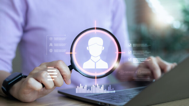 Hand holding a magnifying glass over a digital user profile on a laptop, identity verification, recruitment, data analysis, and online security concept. - Powered by Adobe