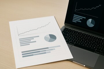 Business report with graphs and charts placed beside a laptop showing matching data visualization on light wood background. Ai generative. Ai generative