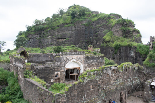 weathered fort ruins of daulatabad nestled at the rocky hill base, partly covered in lush monsoon greenery