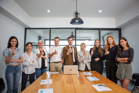 Diverse business team standing together in meeting room with thumbs up, representing teamwork, success, and professional corporate collaboration.