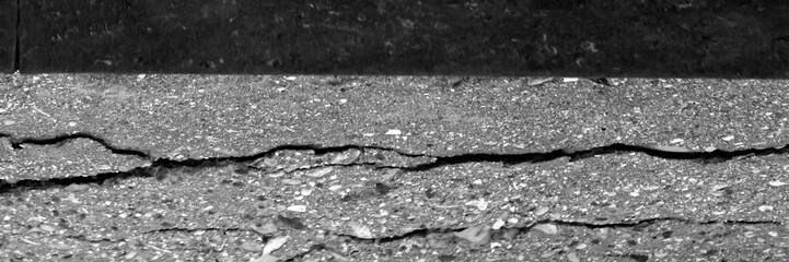 Obraz premium Cracked asphalt road texture. Dark asphalt road texture with cracks, close-up detail perfect for backgrounds, overlays, and construction themes.