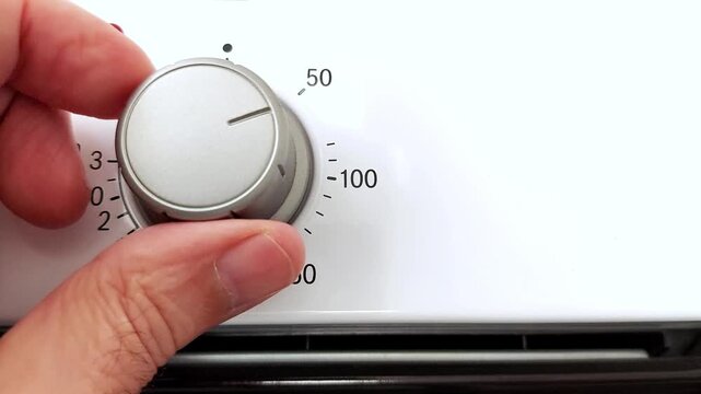 Hand adjusts temperature dial on a modern oven in a bright kitchen. Smooth motion, clear markings, and ambient light show intuitive control in action
