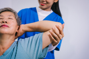 An Asian female nurse provides caring home care to an elderly woman, assisting with arm movement exercises, physical therapy,and rehabilitation to improve joint function, strength,overall well-being