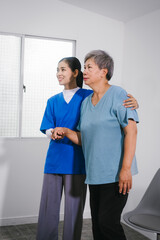 An Asian female nurse provides caring home care to an elderly woman, assisting with arm movement exercises, physical therapy,and rehabilitation to improve joint function, strength,overall well-being
