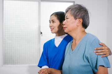 An Asian female nurse provides caring home care to an elderly woman, assisting with arm movement exercises, physical therapy,and rehabilitation to improve joint function, strength,overall well-being
