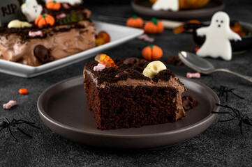 Halloween chocolate cake. Dirty cake with chocolate cream, decorated with worms, skulls, ghosts, pumpkins and sugar sprinkles on a dark background.