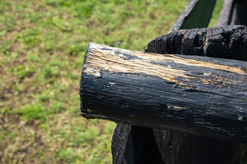 Close-up of a weathered wooden log with a rough texture, showing signs of wear and age. The background features green grass, indicating an outdoor setting.