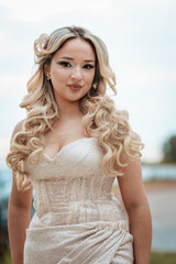 Joyful caucasian woman in a champagne satin prom dress with a high slit, posing outdoors