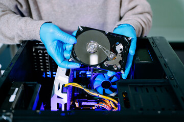 Obraz premium Closeup of technician with gloves holding opened hard drive above computer case, symbolizing data storage, recovery, computer repair, and IT service.