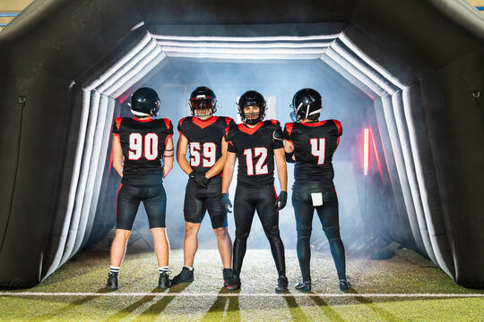 Four american football players in black and red uniforms leaving a smoke filled inflatable tunnel entrance on game day - Powered by Adobe