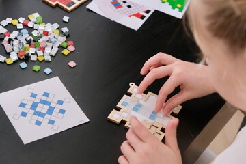 A girl makes a Christmas toy with her own hands from ceramic mosaic. Ceramic mosaic, DIY Christmas tree toy. Eco-friendly toy, educational activity for children.	