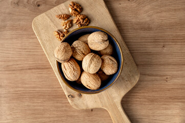 A small bowl with whole walnuts and walnut kernels on a wooden cutting board.