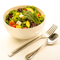 Delicious and vibrant salad with fresh vegetables, avocado, and feta cheese served in a bowl with elegant silverware for a healthy meal concept