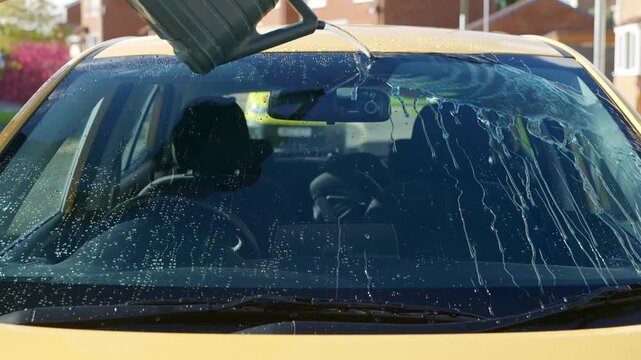 Demonstraing water repelancy of ceramic coating on front window of yellow car water sheeting