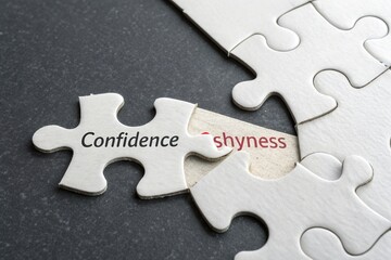 Obraz premium Puzzle pieces labeled 'Confidence' and 'Shyness' on a dark surface, symbolizing personal growth and emotions