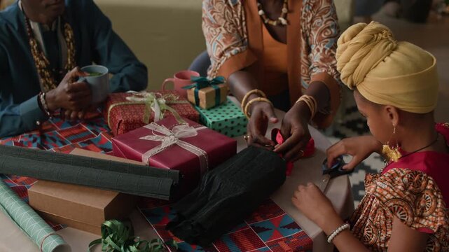 African American family of three wrapping present boxes in colorful paper for Kwanzaa holiday at their living room table, embracing culture and unity